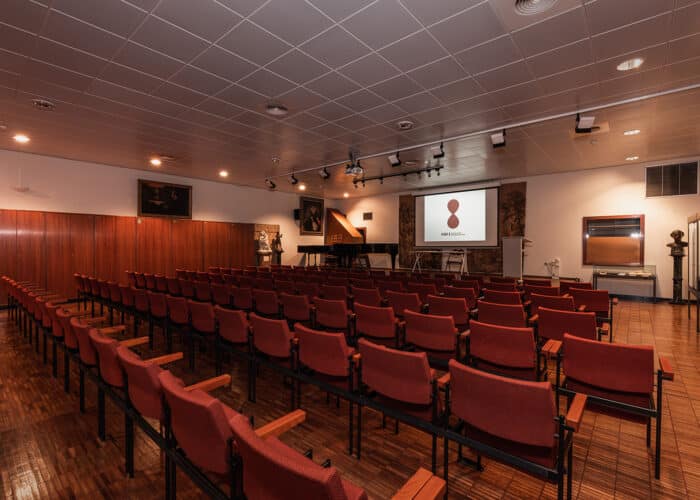 Salle Concert avec piano, estrade, table, chaises, écran et sièges