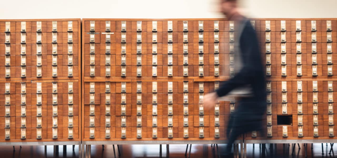 Personne en mouvement passant devant des tiroirs de fiches à KBR