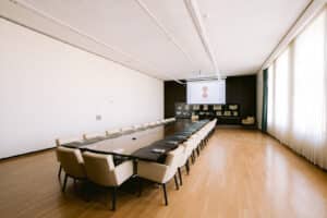 Salle Consilium avec tables et chaises, écran et vitrines