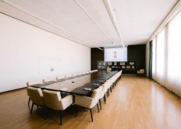 Salle Consilium avec tables et chaises, écran et vitrines